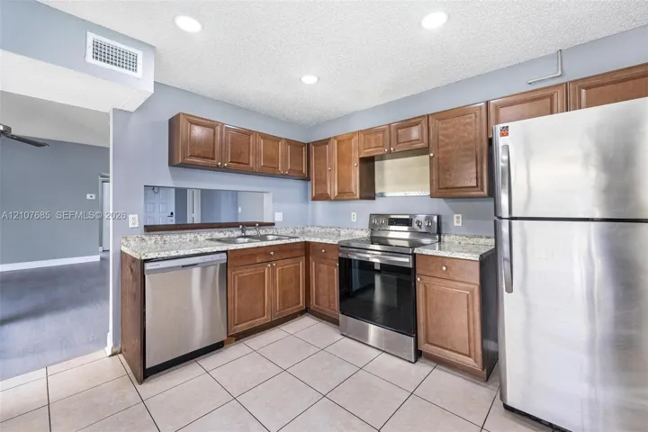 Kitchen featuring medium-toned wood cabinetry, stone-finish countertops, stainless steel appliances, recessed ceiling lighting, and tile flooring