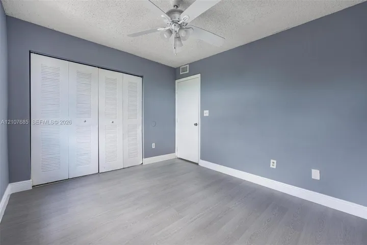 Room featuring wood-finish flooring, four-panel louvered closet doors, and a ceiling-mounted fan with integrated light fixture