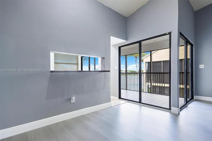 Vaulted ceilings, wood-finish flooring, interior pass-through window with ledge, and floor-to-ceiling sliding glass doors opening to a screened-in balcony
