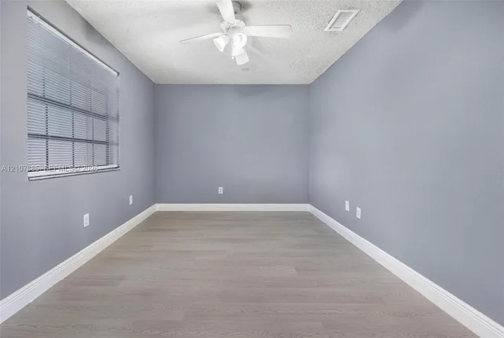 Neutral wall palette featuring wood-finish flooring, a ceiling-mounted fan with integrated light fixture, and horizontal window blinds