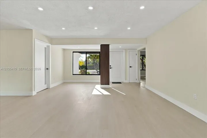 Light-toned wood-finish flooring, recessed ceiling lighting, a dark wood-finish structural pillar, and a large picture window