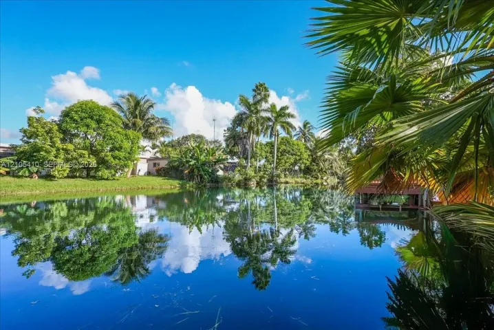 Waterfront property featuring a private dock, lush landscaping with mature palm trees, and expansive green space