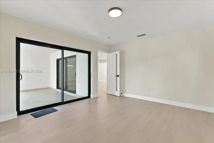 Neutral-toned interior featuring wood-finish flooring, sliding glass doors with black frames, and a modern interior door with glass inlay
