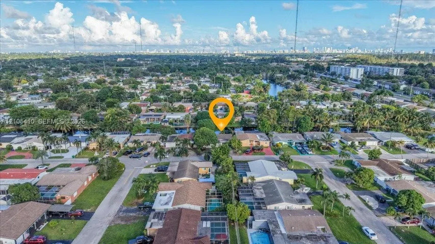 Aerial perspective featuring a waterfront property with a private backyard swimming pool, mature perimeter landscaping, and a multi-car driveway
