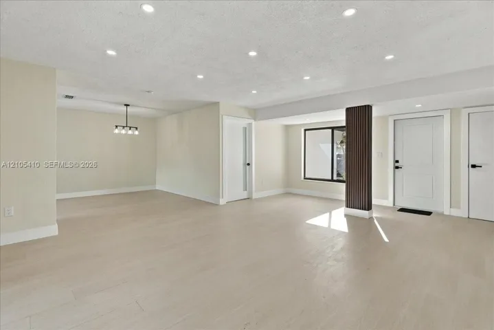 Open-concept interior featuring light wood-finish flooring, recessed lighting, a decorative vertical slat support column, and a modern multi-light chandelier