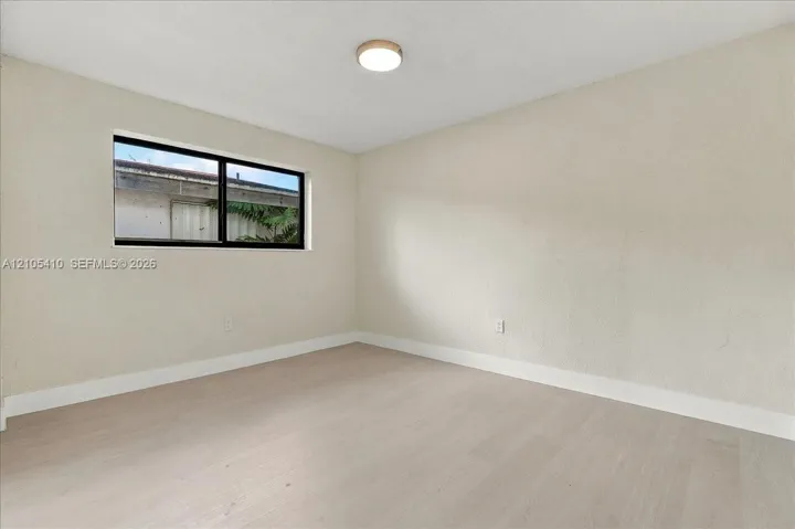 Neutral-toned room featuring wood-finish flooring, a single-pane horizontal window with a dark frame, and a circular flush-mount ceiling light