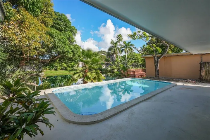 In-ground pool with concrete surround, covered patio space, and mature tropical landscaping set against a water​​‌​​​​‌​​‌‌​‌‌​​​‌‌​‌​‌​‌​​​‌​​ feature
