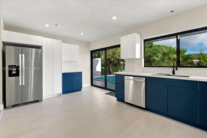 Kitchen featuring dual-tone cabinetry, stainless steel appliances, light-toned wood-finish flooring, quartz countertops, and black fixtures