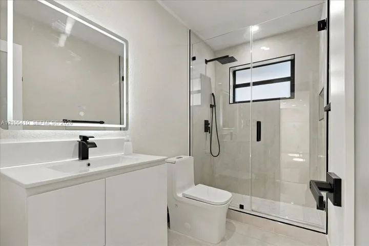 Bathroom featuring a white vanity cabinet, rectangular under-mount sink, integrated LED mirror, walk-in shower with glass enclosure, and matte black hardware