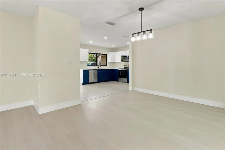 Open interior featuring light-tone wood-finish flooring, a contemporary five-light linear pendant fixture, and a kitchen equipped with dual-tone cabinetry, stainless steel appliances, and tile flooring