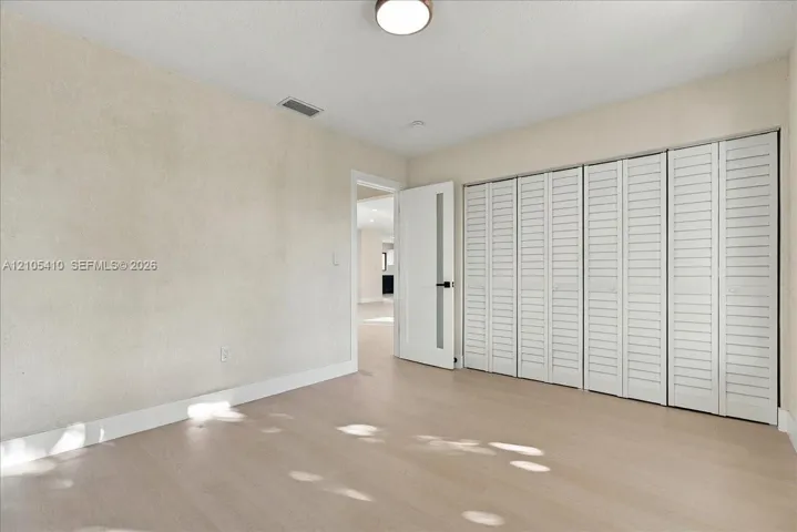 Room featuring light-toned wood-finish flooring, white louvered-panel closet doors, and a single-panel door with a frosted glass insert