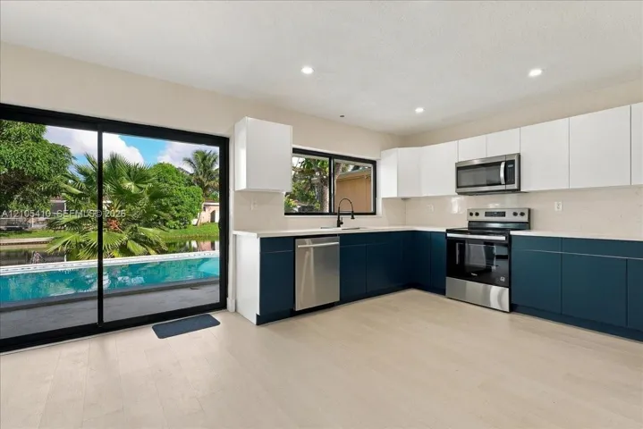 Kitchen featuring two-tone cabinetry, stainless steel appliances, light-toned wood-finish flooring, quartz countertops, and floor-to-ceiling sliding glass doors