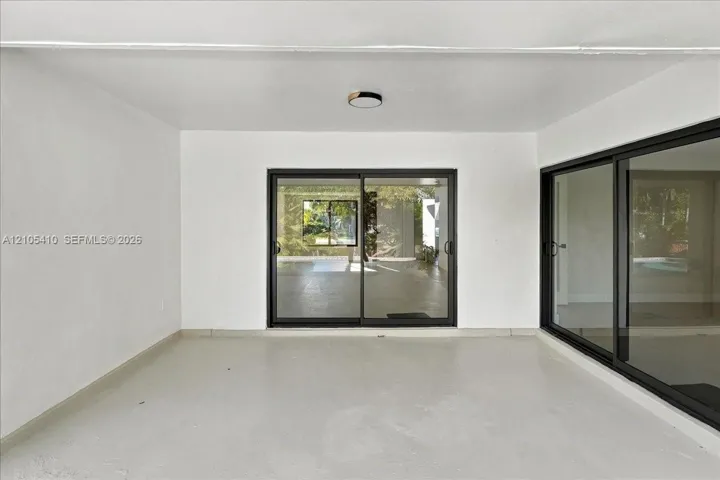 Covered patio featuring concrete flooring, neutral wall finishes, flush-mount ceiling lighting, and black-framed sliding glass doors