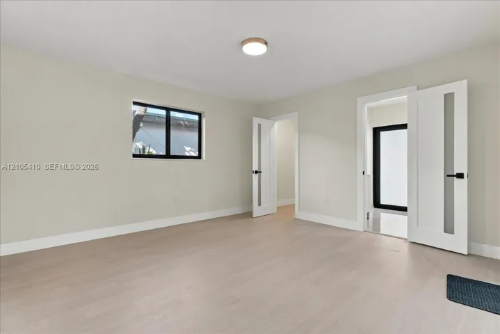 Interior space featuring light wood-finish flooring, neutral wall paint, modern doors with frosted glass panels and matte black hardware, and a flush-mount light fixture