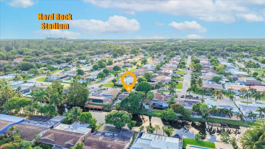 Aerial perspective of a residential neighborhood featuring a canal-front lot, mature palm trees, and residential street infrastructure