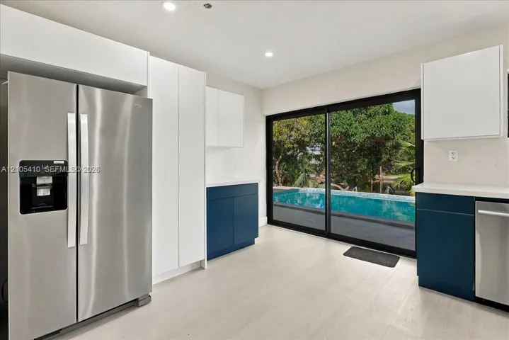 Kitchen featuring white and navy cabinetry, stainless steel appliances, light wood-finish flooring, and sliding glass doors with a perspective of an outdoor pool