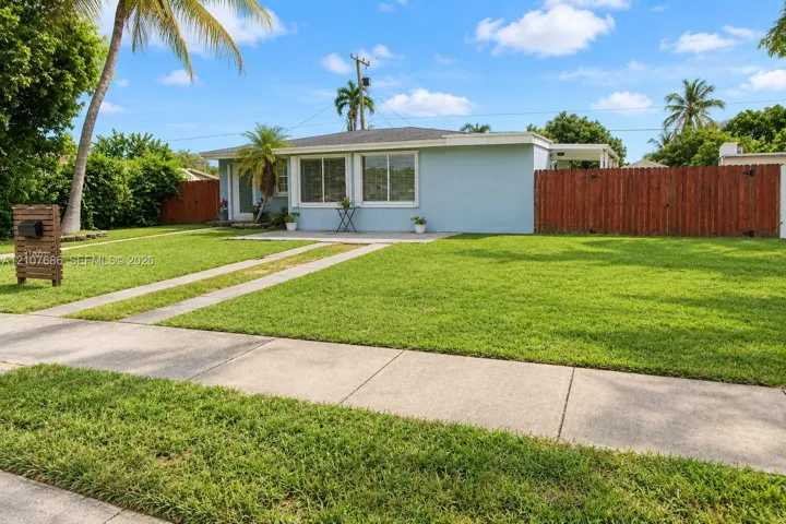 Single-story residence featuring light-toned exterior siding, a paved concrete driveway, a front patio area, and a wood privacy fence