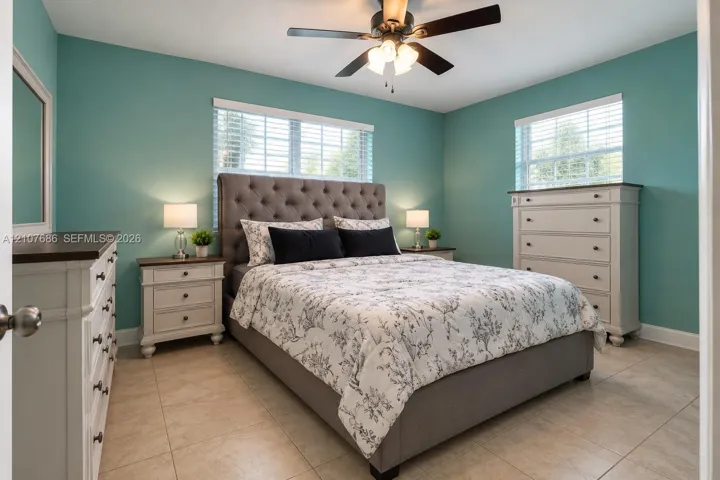 Neutral-toned tile flooring, dual windows with horizontal blinds, and a central ceiling fan with integrated lighting