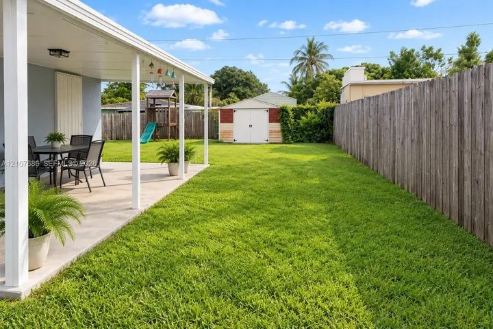 Covered concrete patio with white support columns, fenced backyard, and detached storage shed
