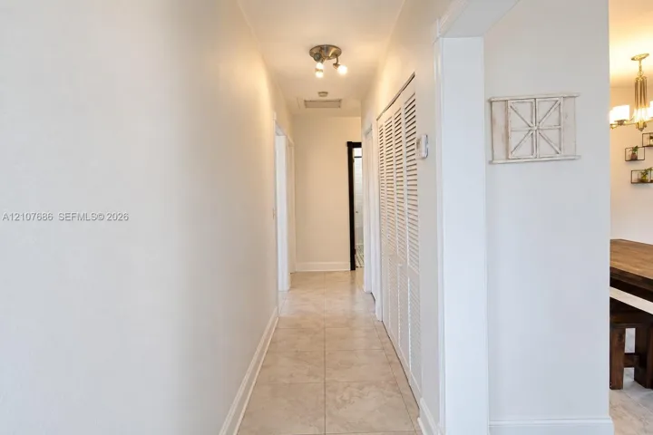 Hallway featuring neutral tile flooring, louvered closet doors, and a multi-bulb flush-mount ceiling fixture