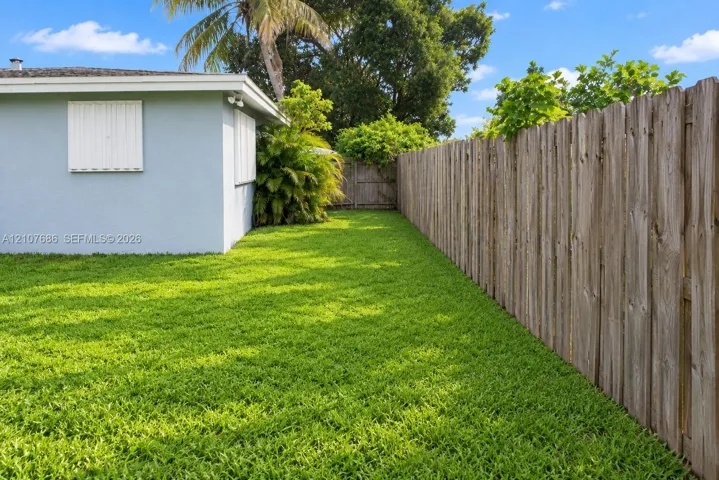 Private backyard featuring a manicured lawn, wood-panel fencing, exterior wall-mounted shutters, and mature landscaping