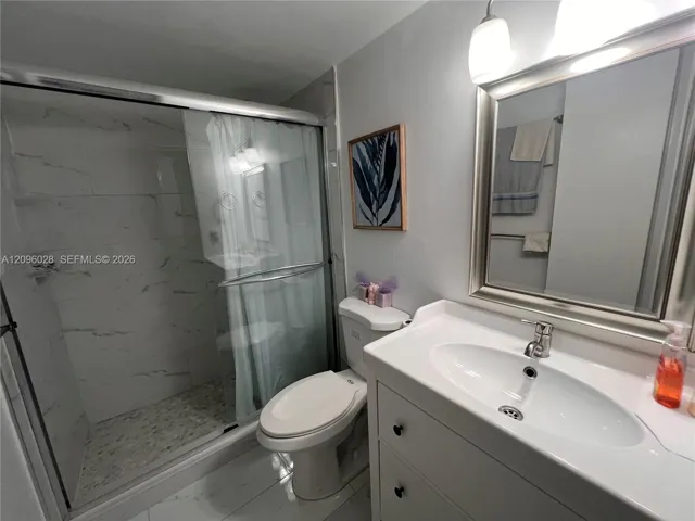 Bathroom featuring a vanity with an integrated sink, polished chrome faucet, framed mirror, walk-in shower with sliding glass doors and wall tile, and large-format tile flooring