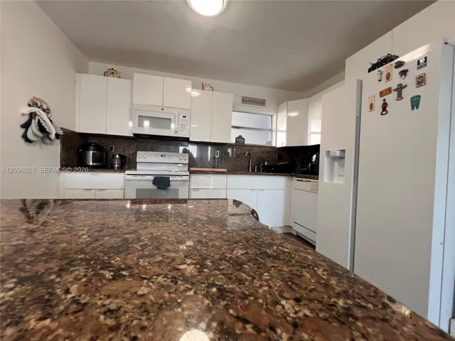 Kitchen featuring white cabinetry, stone-finish countertops, an island, and integrated white appliances