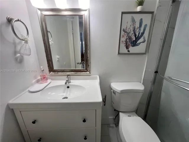 White vanity with an integrated basin, brushed metal hardware, wall-mounted mirror, overhead light fixture, and walk-in shower with sliding glass doors