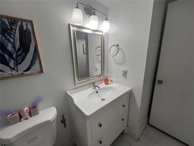Vanity with integrated porcelain sink, three-light polished chrome fixture, framed wall mirror, and ring towel holder