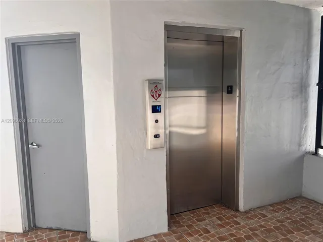 Stainless steel elevator with a digital floor indicator and push-button controls, accompanied by a solid-core door and terracotta-tone tiled flooring