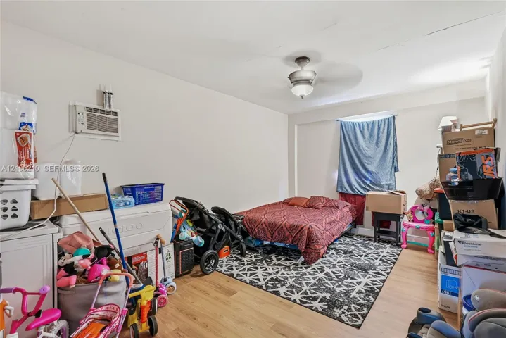 Interior room featuring light wood-finish flooring, a ceiling fan with integrated lighting, and a wall-mounted air conditioning unit