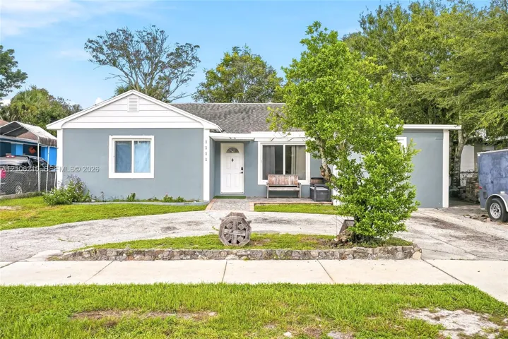 Single-story exterior featuring a grey smooth-finish facade, white horizontal gable siding, a pitched asphalt shingle roof, and a paved stone walkway