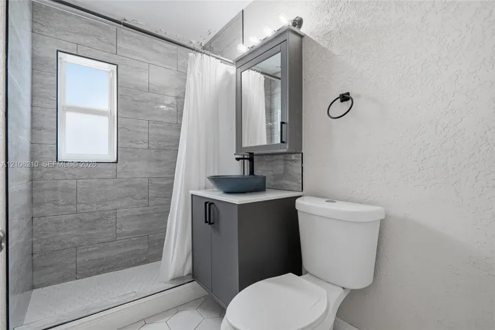 Bathroom featuring a walk-in shower with grey horizontal tile surround, grey vanity cabinet, vessel sink, and mirrored medicine cabinet
