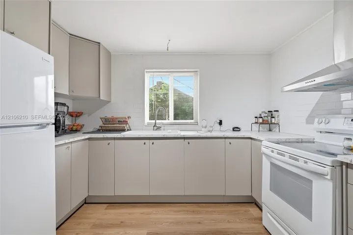 Kitchen featuring light gray flat-panel cabinetry, white solid surface countertops, a stainless steel range hood, and wood-finish flooring