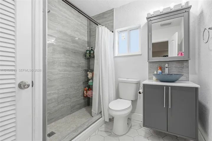 Bathroom featuring a shower stall with stone-finish tile surround, vanity with a vessel sink, integrated medicine cabinet, and white hexagonal floor tile