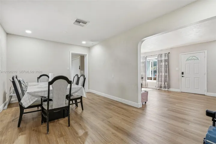 Open-concept interior featuring wood-finish flooring, recessed lighting, and a prominent arched entryway leading to the exterior entrance door