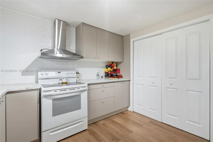 Kitchen featuring flat-panel cabinetry, stone-finish countertops, white subway tile backsplash, stainless steel chimney-style range hood, and wood-finish flooring