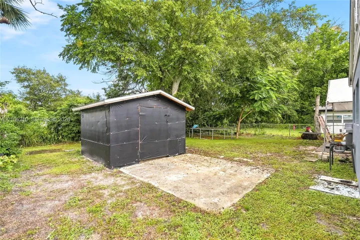 Backyard area featuring a structural storage shed, concrete foundation pad, chain-link fencing, and mature trees