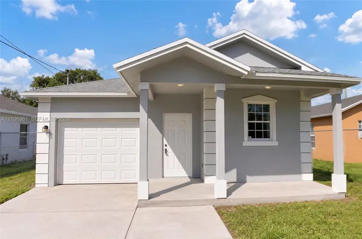 Single-story exterior featuring light-toned stucco siding, decorative corner quoins, a covered front porch with square columns, and an integrated single-car garage