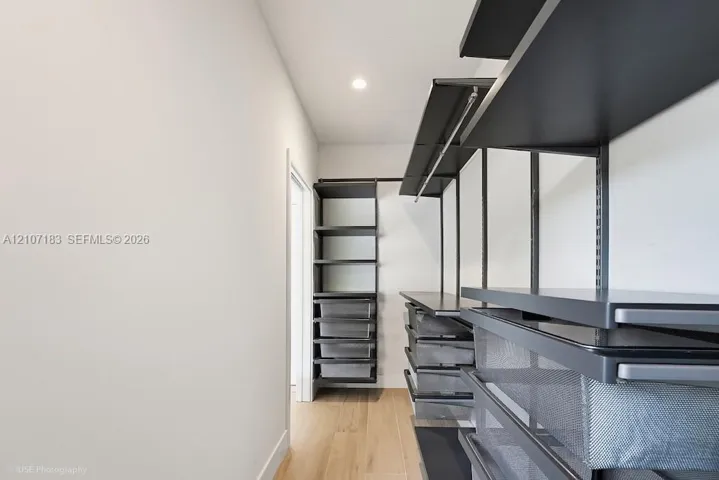 Custom storage system featuring matte black metal shelving, integrated pull-out wire baskets, hanging rods, and wood-finish flooring