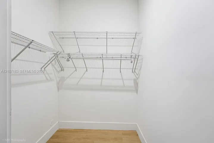 Walk-in storage space featuring multi-tiered white wire shelving, integrated hanging rods, and wood-finish flooring