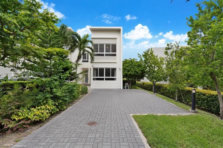 Contemporary architectural exterior with smooth white stucco facade, multi-level horizontal windows, and a paved brick driveway