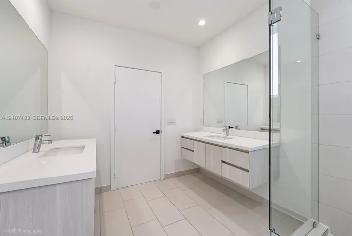 Floating dual vanities with white countertops and undermount sinks, full-width wall mirrors, large-format tile flooring, and a walk-in glass-enclosed shower