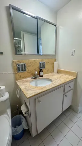 Vanity featuring a stone-patterned countertop, integrated undermount sink, white cabinetry with polished knobs, and a large-format metallic-framed medicine cabinet