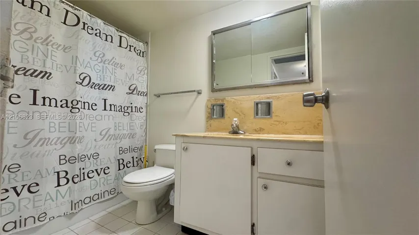 Bathroom featuring a vanity with neutral stone-style countertop, integrated sink, large wall-mounted mirror, and tiled flooring