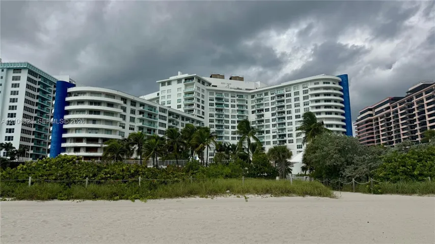 Multi-story high-rise building featuring curved architectural lines, private balconies, and direct access to a sandy beach