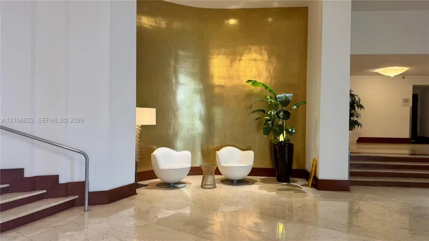 Curved gold-tone feature wall with high-gloss finish, polished stone flooring, and metal handrail
