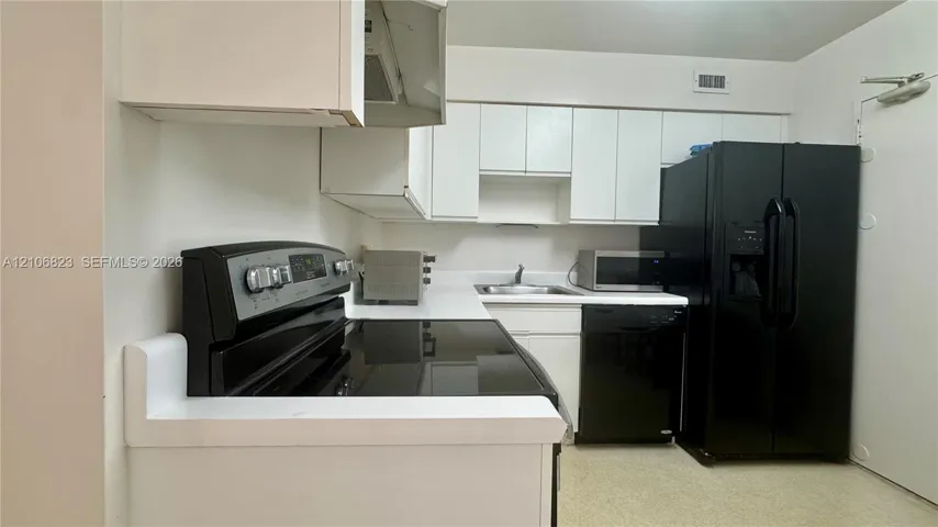 Kitchen featuring white cabinetry, contrasting black appliances, solid-surface countertops, and a dual-basin sink