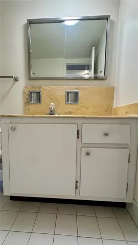 White vanity cabinet with chrome hardware, natural stone countertop with matching backsplash, dual inset soap dishes, and a framed mirror