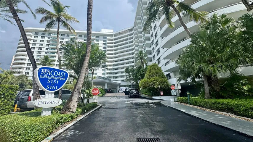 Mid-rise residential building with wrap-around balconies, porte-cochère entrance, and mature tropical landscaping